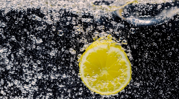 Photo sous l'eau de limonade sucrée fraîchement pressée dont les tranches de citrons crus tombent dans l'eau gazeuse sur fond bleu foncé ou noir gros plan sur la limonade ou le cocktail de citron highball boisson rafraîchissante froide