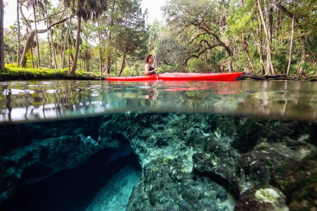 Sur et sous photo d'une fille faisant du kayak dans un lac près d'une formation de grottes sous-marines