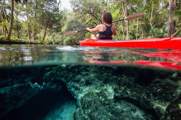 Sur et sous photo d'une fille faisant du kayak dans un lac près d'une formation de grottes sous-marines