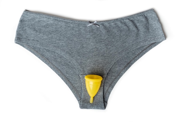 Sous-vêtements féminins culottes grises et coupe menstruelle jaune sur fond blanc Concept de santé des femmes Eco friendly