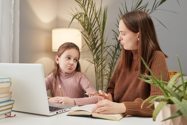 Soutien à l'enseignement à distance pour les parents Mère triste et fille contrariée utilisant l'ordinateur portable pour faire leurs devoirs se sentant indifférentes aux matières scolaires dans l'intérieur de la maison