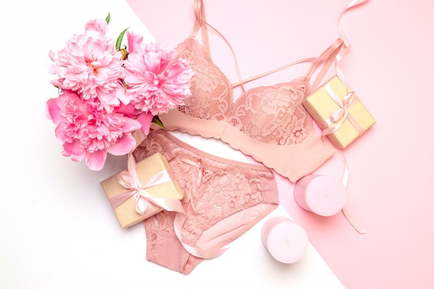 Soutien-gorge et culotte femme en dentelle rose élégante, bougies roses fleurs, un bouquet de belles pivoines, cadeaux