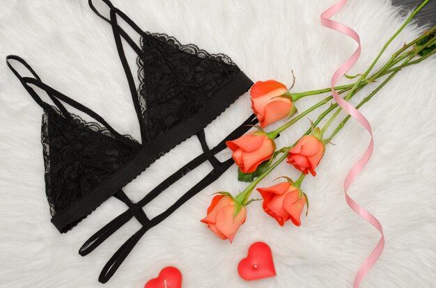 Photo soutien-gorge en dentelle noire sur fourrure blanche et un bouquet de roses orange