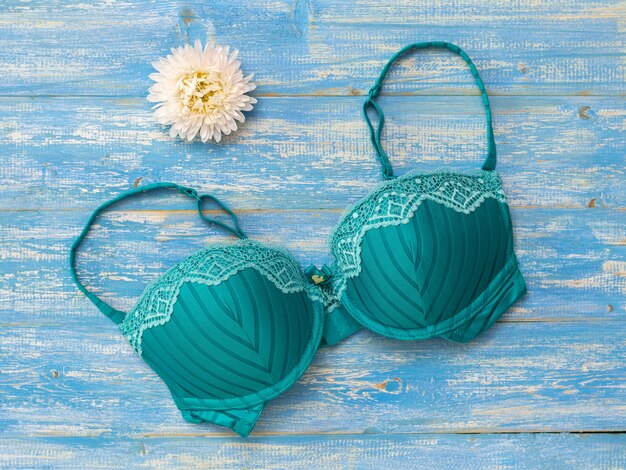 Soutien-gorge vert avec fleur blanche sur table en bois bleue. Sous-vêtements sexy pour femmes.