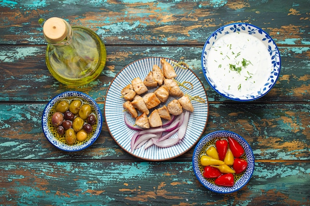 Photo souvlaki grec à la viande sur assiette sur fond de bois rustique d'en haut, servi avec de l'huile d'olive en bouteille, du tzatziki et d'autres apéritifs traditionnels de grèce