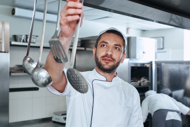 Photo soyez sûr que le cuisinier choisit des ustensiles pour cuisiner dans la cuisine du restaurant