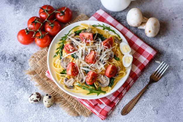 Spaghetti aux champignons, fromage, épinards, rukkola et tomates cerises. Plat italien, culture méditerranéenne