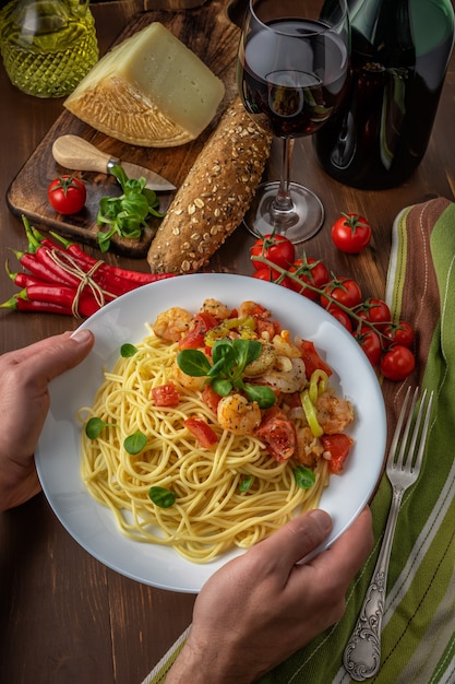 Spaghetti aux crevettes, tomates cerises et épices sur fond en bois.