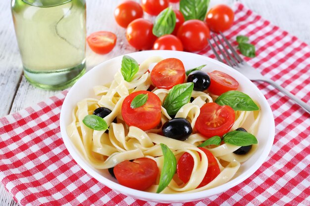 Spaghetti aux olives tomates et feuilles de basilic sur plaque sur serviette sur fond de bois