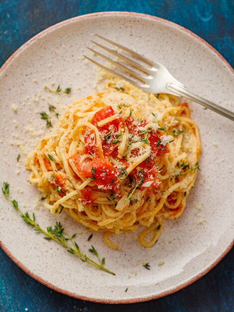 Spaghetti aux tomates et au thym dans une assiette sur une table bleue, vue de dessus