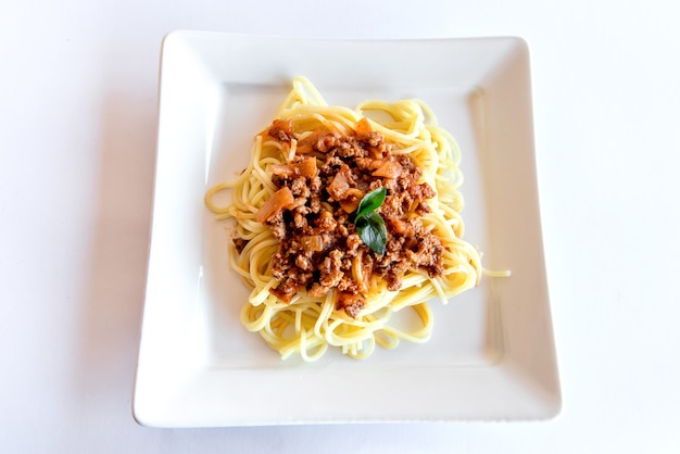 Spaghetti bolognaise servi sur une assiette blanche sur fond blanc avec basilic, vue de dessus.