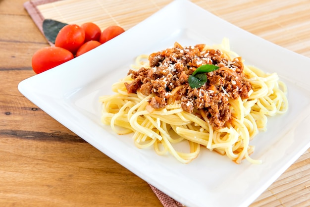 Spaghetti bolognaise servi sur une assiette blanche sur un fond en bois avec des tomates et du basilic.