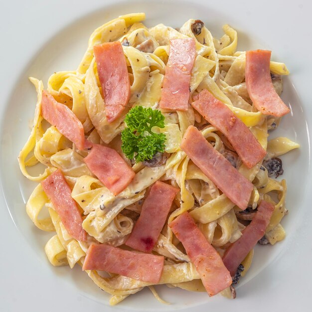 Photo spaghetti à la crème aux champignons avec du jambon sur un plat blanc mis sur la table boisée dans un restaurant italien