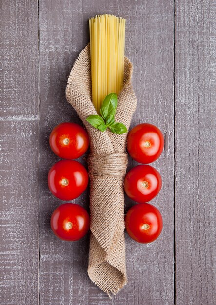 Spaghetti cru en toile de lin avec tomates et basilic sur table en bois