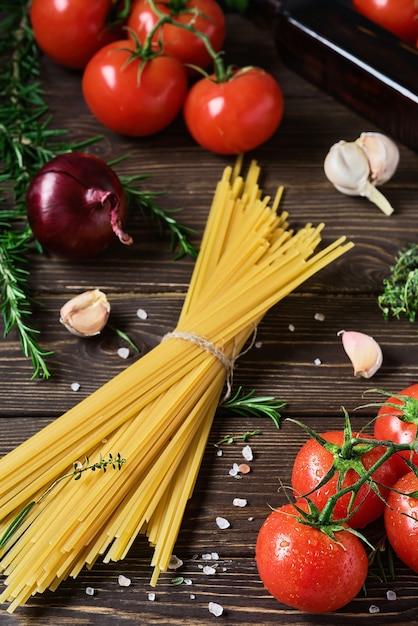 Spaghetti à grains entiers avec des ingrédients pour la cuisson du déjeuner de style italien sur une table en bois sombre. L'idée de cuisiner des pâtes. Gros plan, mise au point sélective