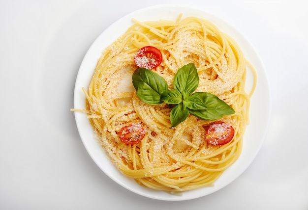 Spaghetti italien aux tomates cerises, basilic et parmesan sur une assiette blanche. Vue d'en-haut