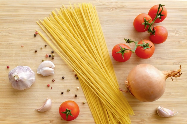 Spaghetti non cuits avec tomates cerises et oignons en grains de poivre à l'ail sur une planche à découper