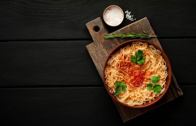 Spaghetti de pâtes italiennes appétissantes avec sauce tomate, parmesan sur une plaque, planche à découper sur un fond de bois. Vue d'en-haut