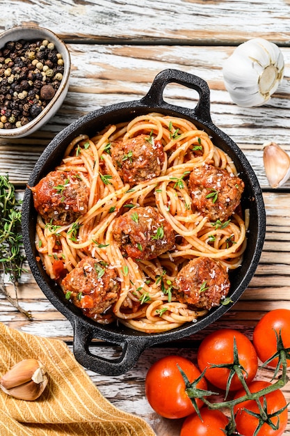 Spaghetti de pâtes italiennes à la sauce tomate et boulettes de viande dans une poêle en fonte avec du parmesan. Fond en bois blanc. Vue de dessus