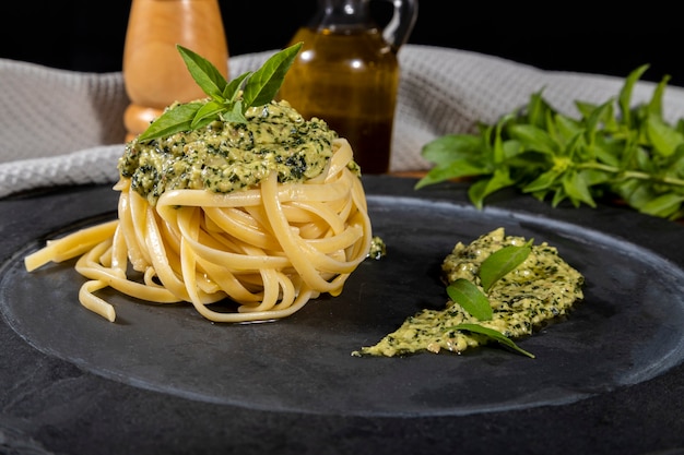 Spaghetti de pâtes avec sauce pesto et feuilles de basilic frais dans un plat en pierre noire sur fond de bois.