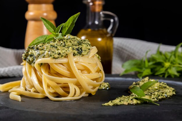 Spaghetti de pâtes avec sauce pesto et feuilles de basilic frais dans un plat en pierre noire sur fond de bois.