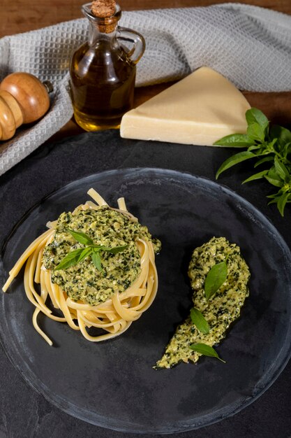 Spaghetti de pâtes avec sauce pesto et feuilles de basilic frais dans un plat en pierre noire sur fond de bois.