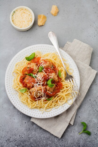 Spaghetti de pâtes à la sauce tomate, parmesan, basilic et boulettes de viande sur plaque en céramique blanche sur béton gris ou surface en pierre. Mise au point sélective.