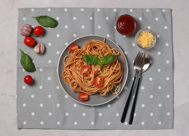 Spaghetti à la sauce tomate et tomates cerises au basilic sur assiette et serviette grise.