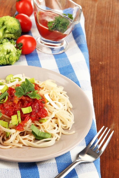 Spaghetti savoureux avec sauce et légumes sur plaque sur table en bois libre