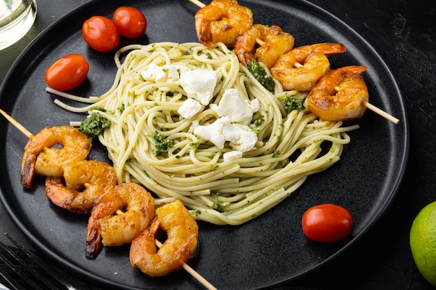 Spaghetti vert avec sauce pesto et brochettes de crevettes grillées, sur plaque, sur fond noir