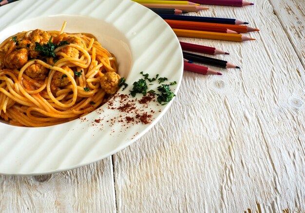 Photo des spaghettis avec des boulettes de poulet et de la sauce tomate avec des crayons de couleur sur la table.