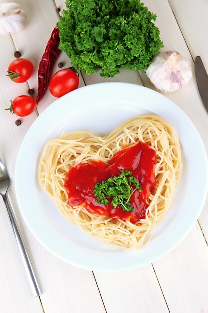 Spaghettis cuits soigneusement disposés en forme de coeur et garnis de sauce tomate, sur fond de bois