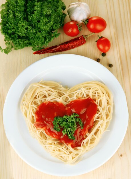 Spaghettis cuits soigneusement disposés en forme de coeur et garnis de sauce tomate, sur fond de bois