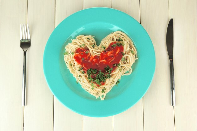 Spaghettis cuits soigneusement disposés en forme de coeur et garnis de sauce tomate, sur fond de bois