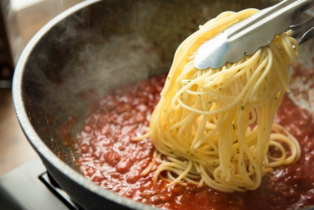 Des spaghettis sont mis dans la casserole avec de la sauce bolognaise chaude