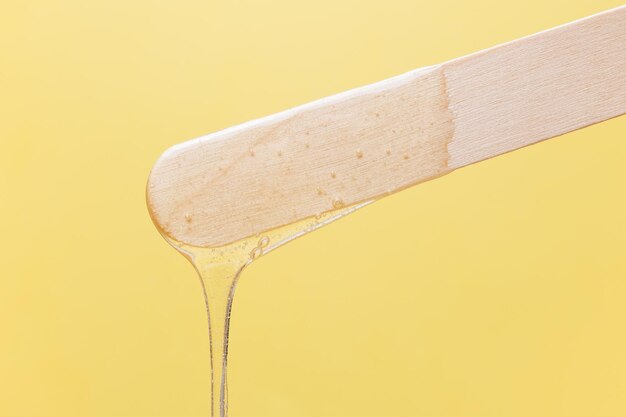 Photo spatule en bois avec pâte de sucre liquide pour l'épilation sur fond jaune épilation épilation