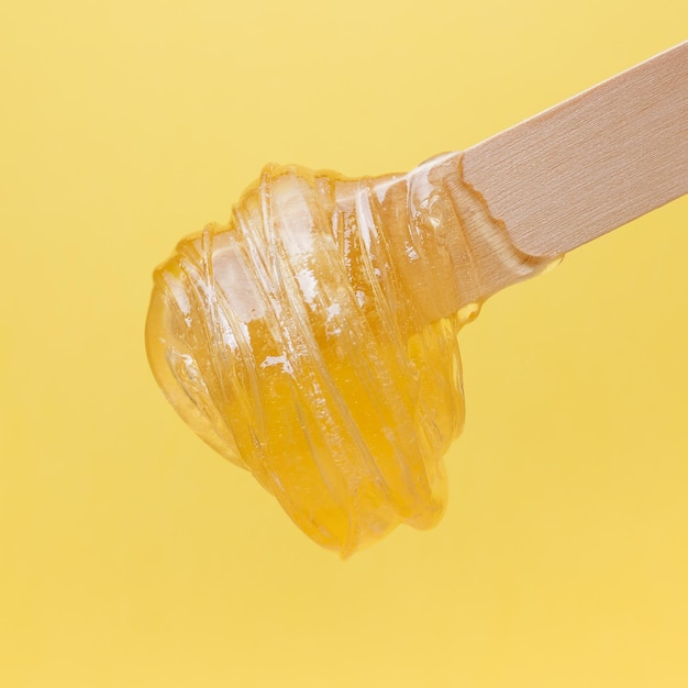 Spatule en bois avec pâte de sucre liquide pour l'épilation sur fond jaune Épilation épilation