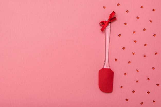 Spatule de cuisine décorée de ruban rouge avec des étoiles sur fond rose. Outils de cuisine sur fond festif. Mise à plat.