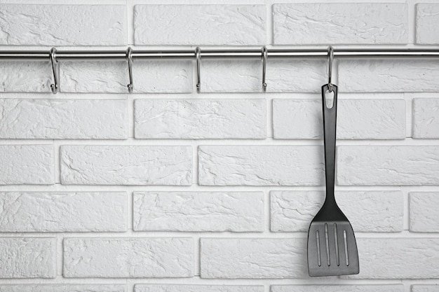 Spatule noire accrochée au rack contre le mur de briques