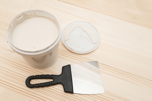 Spatule et un seau de mastic blanc sur des planches en bois