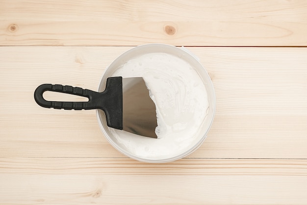 Spatule et un seau de mastic blanc sur des planches en bois