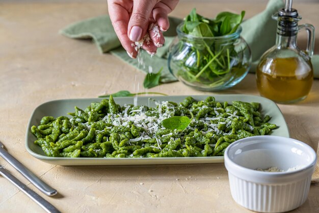 Les spatzles aux épinards sont les boulettes ou les gnocchis verts typiques du Tyrol sur une assiette verte avec du fromage râpé