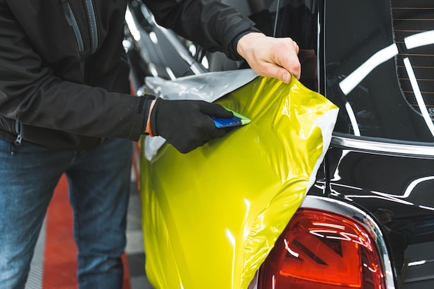 Un spécialiste de l'automobile enveloppant un film vinyle jaune fluo sur une voiture noire à l'atelier de réparation