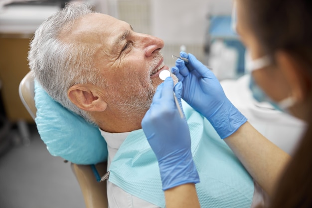 Spécialiste dentaire professionnel tenant un miroir buccal et un cure-dent lors de l'examen d'un homme âgé