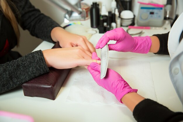 Le spécialiste de la manucure dans les gants en caoutchouc travaille avec de la lime à ongles. Salon de beauté.