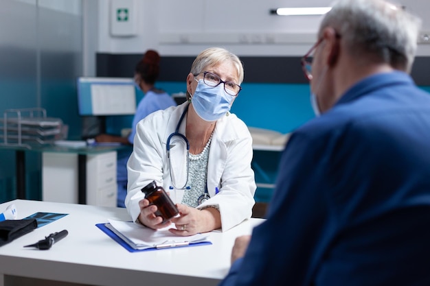 Spécialiste médical tenant une bouteille de pilules à donner à un homme âgé pendant la pandémie de covid 19. Médecin donnant un pot avec un traitement sur ordonnance et des médicaments à un patient malade portant un masque facial.