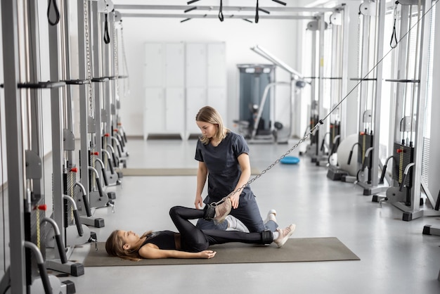 Spécialiste de la réadaptation aidant une petite fille à faire des exercices sur des simulateurs au gymnase