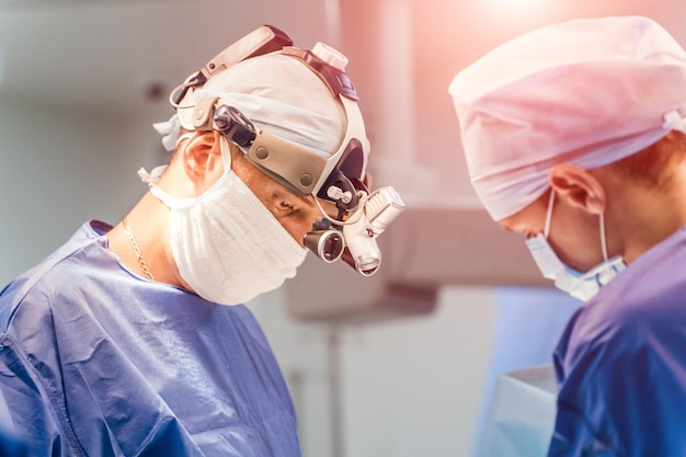 Des spécialistes en uniforme médical font une opération à l'hôpital Un chirurgien avec une loupe sur la tête travaille avec des assistants dans la salle d'opération