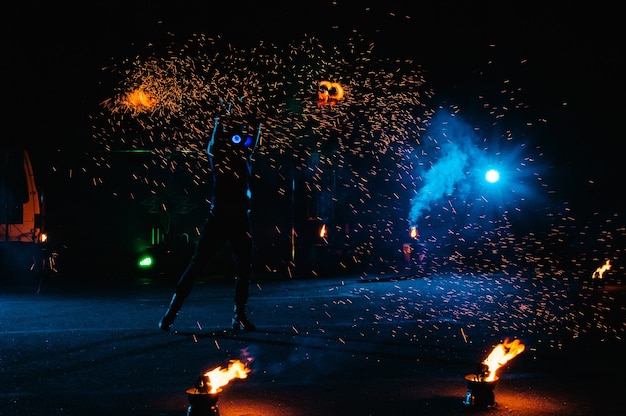 Spectacle de feu, danse avec la flamme, maître masculin jonglant avec des feux d'artifice, performance en plein air, dessine une silhouette enflammée dans l'obscurité, des étincelles lumineuses dans la nuit. Un homme en costume LED danse avec le feu.