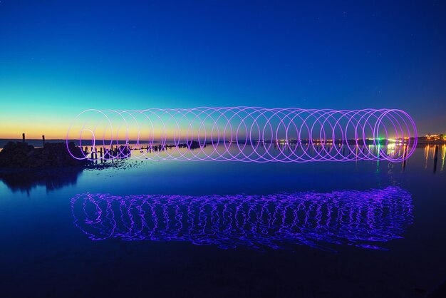 Spectacle de feu laser incroyable dans le ciel bleu nuit avec des reflets dans l'eau de mer